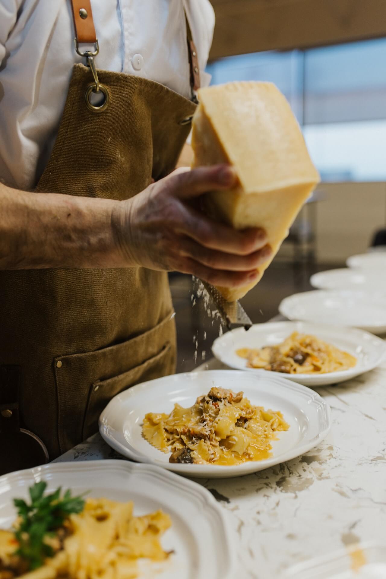 Chef grating parmesan over plates of fresh pasta
